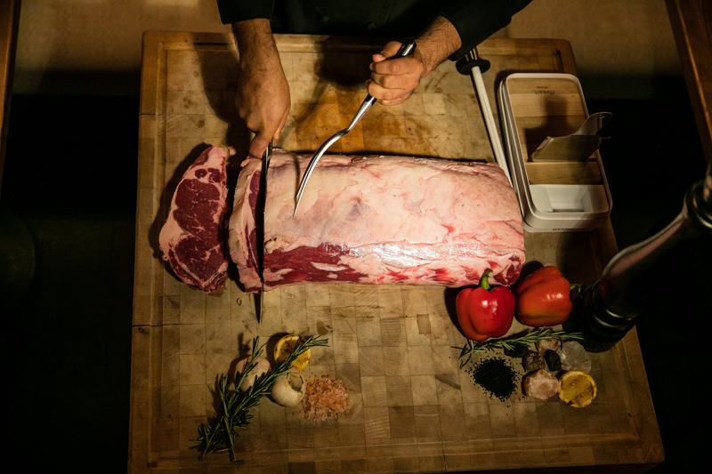 meat-being-cut-on-wooden-board-with-red-peppers-garlic-parsley-and-lemon--on-side